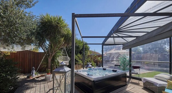 Un bain à remous situé dans un espace extérieur abrité, doté d’une terrasse en bois, d’une pergola et offrant une vue sur un paysage naturel.