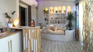 A modern interior with a wooden counter, a sofa with cushions, a shelf with items, and a decorative wall. - Gîte Escale Bien Etre in Biscarrosse (Biscarrosse)