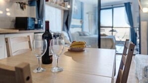 A dining table with two wine glasses and a bottle, a plate with bananas, and a view of a room with a bed and a window.