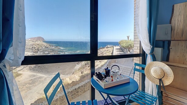 A room with a view of the sea, a table with a tray of items, and a straw hat.