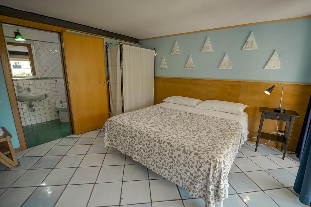 A bedroom with a bed, a nightstand, a bathroom with a sink and toilet, and a shower area.
