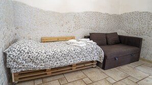 A room with a bed, a wooden headboard, a brown sofa, and a stone wall. - b&b Domus Vesuvia (Torre Annunziata)