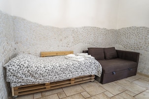 Una habitación con una cama, cabecera de madera, un sofá marrón y una pared de piedra.