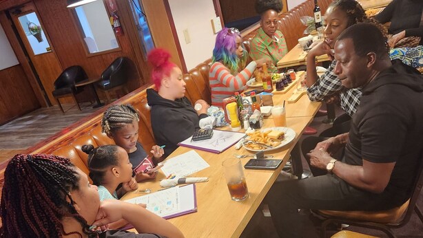 A group of people seated around a long wooden table in a restaurant with leather booths and pendant lighting. - Delta Queen Lodge Bar Restaurant (Isleton)