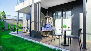 Un patio moderno al aire libre con una hamaca colgante, dos mesas con sillas y una pequeña planta en maceta.