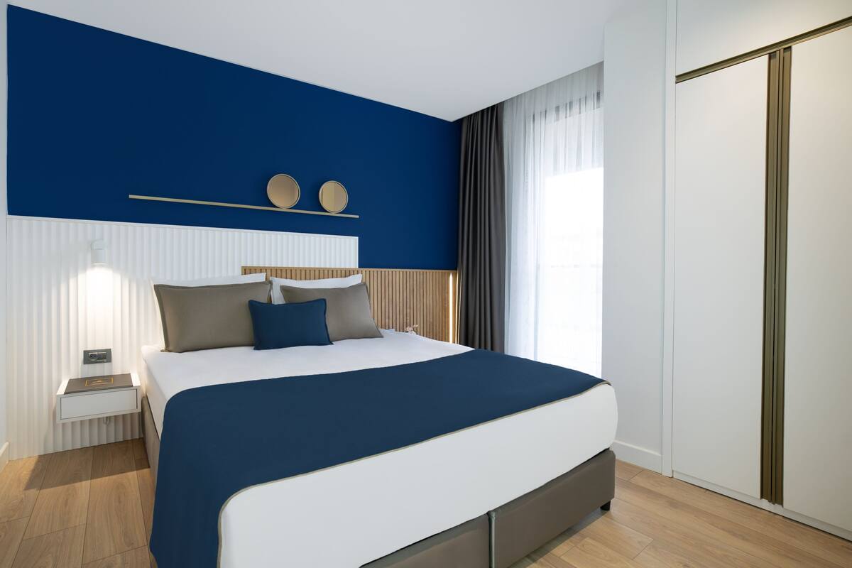 A modern bedroom with a large bed, a bedside table, a nightstand, a wardrobe, and a window with curtains.
