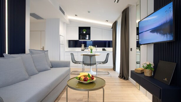 Una sala moderna con un sofá, una mesa de comedor con fruta, una cocina al fondo y un televisor en la pared.