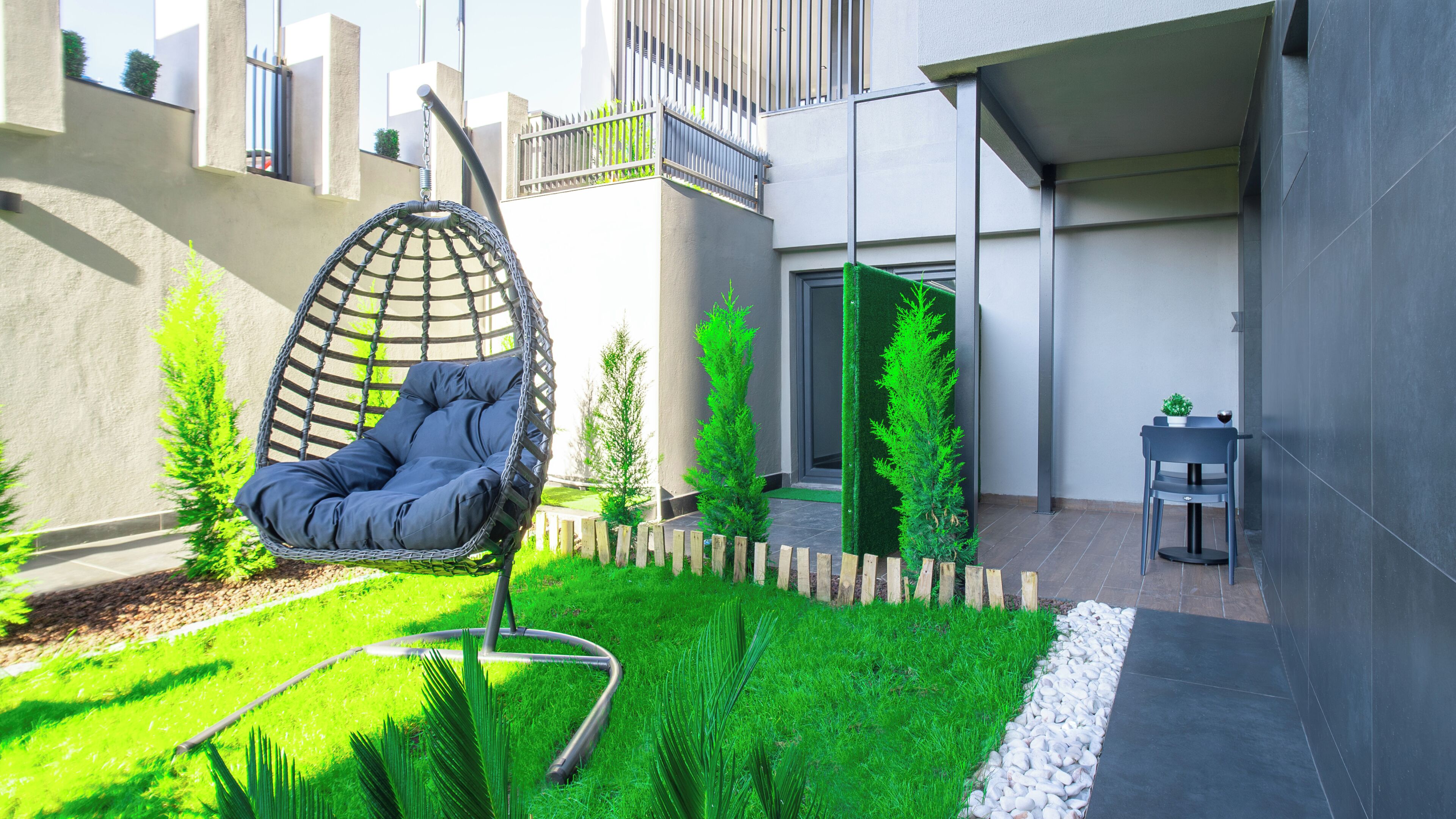 A modern outdoor seating area with a hanging chair, a small table, and a potted plant.