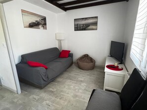A compact living space with a grey sofa, a bean bag, a desk with a TV, and two wall-mounted pictures.