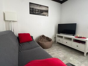 A room with a grey sofa, a red pillow, a television on a white stand, and a picture on the wall.