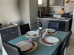 A dining area with a table set for four, a bottle of wine, and a kitchen in the background.