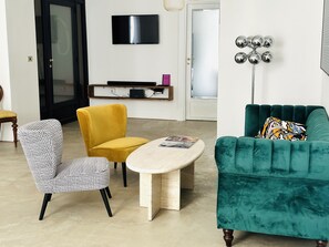 A living room with a teal sofa, a yellow armchair, and a patterned armchair. A flat-screen TV is mounted on the wall, and a floor lamp is visible. - Historical building in the heart of the city center  (Napoli)