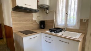 Pieni, käytännöllinen keittiö, jossa on työtaso, pesuallas, kaappeja ja ikkuna, jossa on verhot.