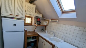 A compact kitchen with a refrigerator, stove, sink, and wooden cabinets.