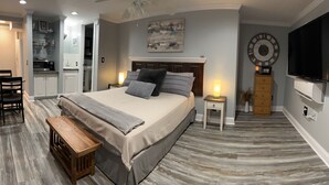 A bedroom with a large bed, bedside tables, a TV, and a kitchen area visible through an open door. - Thomas Mill Creek Lakefront Property  (Abbeville)