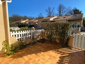 A courtyard with terracotta tiles, a white picket fence, and a building with a tiled roof. - Charming air-conditioned pavilion with pool, near beach (Argelès-sur-Mer)