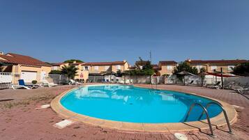 A swimming pool with a metal ladder, surrounded by a brick patio, and adjacent to a row of houses with tiled roofs.