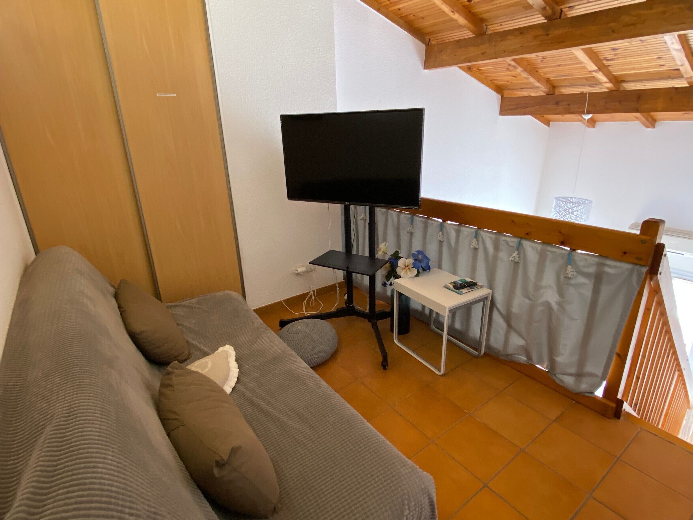 Een kamer met een bank, een televisie op een standaard, een kleine tafel met een bloevas en een raam met gordijnen.