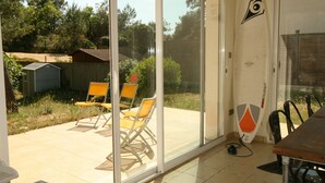 Een kamer met een glazen schuifdeur die uitkomt op een terras met stoelen en een surfplank.