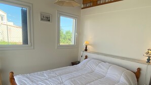 Een slaapkamer met een groot bed, twee ramen, een nachtkastje met een lamp en een foto aan de muur.