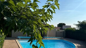 Uma piscina cercada por um pátio de tijolos, com folhagem verde exuberante em primeiro plano.