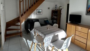 Uma área de refeições com mesa, cadeiras, escada, sofá, televisão e estante de livros.