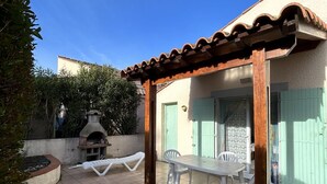 Um pátio externo com pérgola de madeira, forno de pedra e mesa com cadeiras.