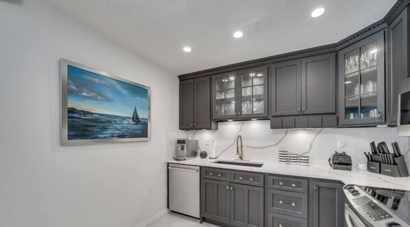 A modern kitchen with grey cabinets, a built-in dishwasher, and a painting of a sailboat on the wall.