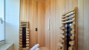 Een houten sauna met banken en een houten bank, een handdoek op de vloer, en een houten deur met een handvat.