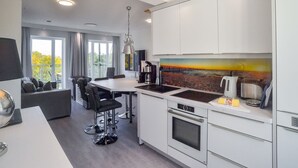 Een moderne keuken met witte kasten, een inbouwoven en een groot kookeiland met barkrukken.