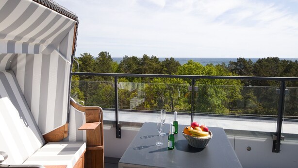 Een balkon met uitzicht op zee, een tafel met een fruitschaal en een streepstoel.