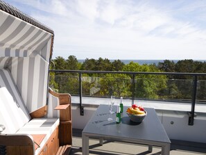 A balcony with a view of the sea, a table with a fruit basket, and a striped chair.