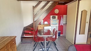 A dining area with a table and chairs, a kitchen area with a microwave and a clock, and a staircase leading to another level.