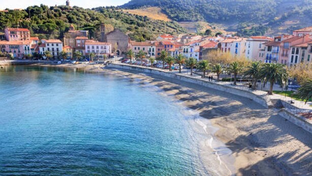A coastal town with a clear blue sea, a sandy beach, and buildings with red roofs.