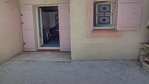 A narrow entrance with a door labeled '71' leading inside. A bicycle is parked inside, and a window with shutters is visible on the right.