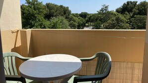 A balcony with a table and chairs, overlooking a park with trees and a pathway. - Bright studio with balcony, Wi-Fi, air conditioning, near park (Balaruc-les-Bains)
