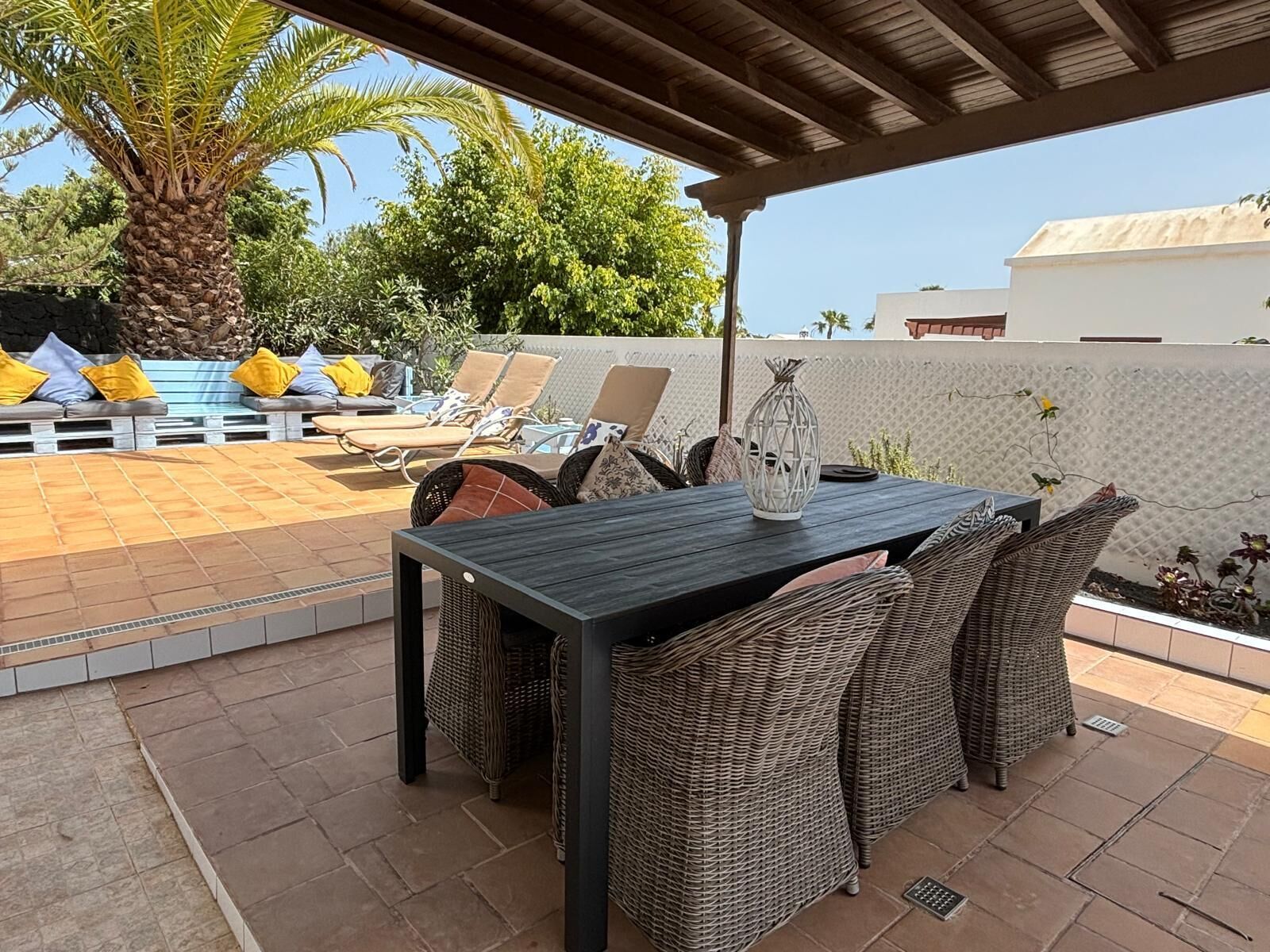 Un patio al aire libre con una mesa, sillas de mimbre, piscina y sillones de descanso.