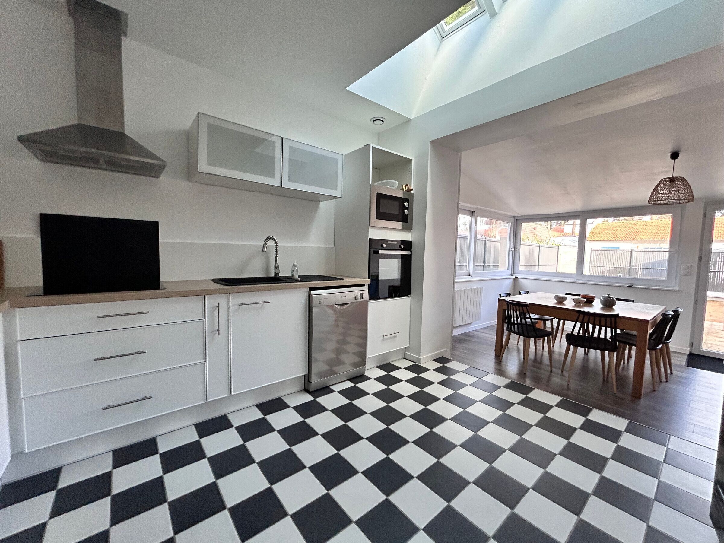 A modern kitchen with a black and white checkered floor, white cabinetry, and a dining area with a table and chairs.