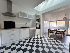 Une cuisine moderne avec un sol à carreaux noirs et blancs, des meubles blancs et un coin repas comprenant une table et des chaises.