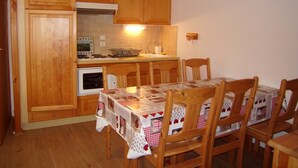 A compact kitchen with wooden cabinets, a stove, and a dining table with chairs. - Cozy 2-Bedroom Apartment for 4 with Terrace, Parking, and Modern Amenities in Crest-Voland (Crest-Voland)