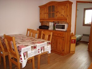 A dining area with a wooden table and chairs, a wooden cabinet with a microwave, and a small kitchenette.