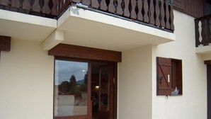 A building with a wooden balcony, a glass door entrance, and a small window with shutters. - Cozy 2-Bedroom Apartment for 4 with Terrace, Parking, and Modern Amenities in Crest-Voland (Crest-Voland)