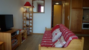 A cozy living room with a wooden sofa, a TV, a lamp, and a bookshelf. - Cozy 2-Bedroom Apartment for 4 with Terrace, Parking, and Modern Amenities in Crest-Voland (Crest-Voland)