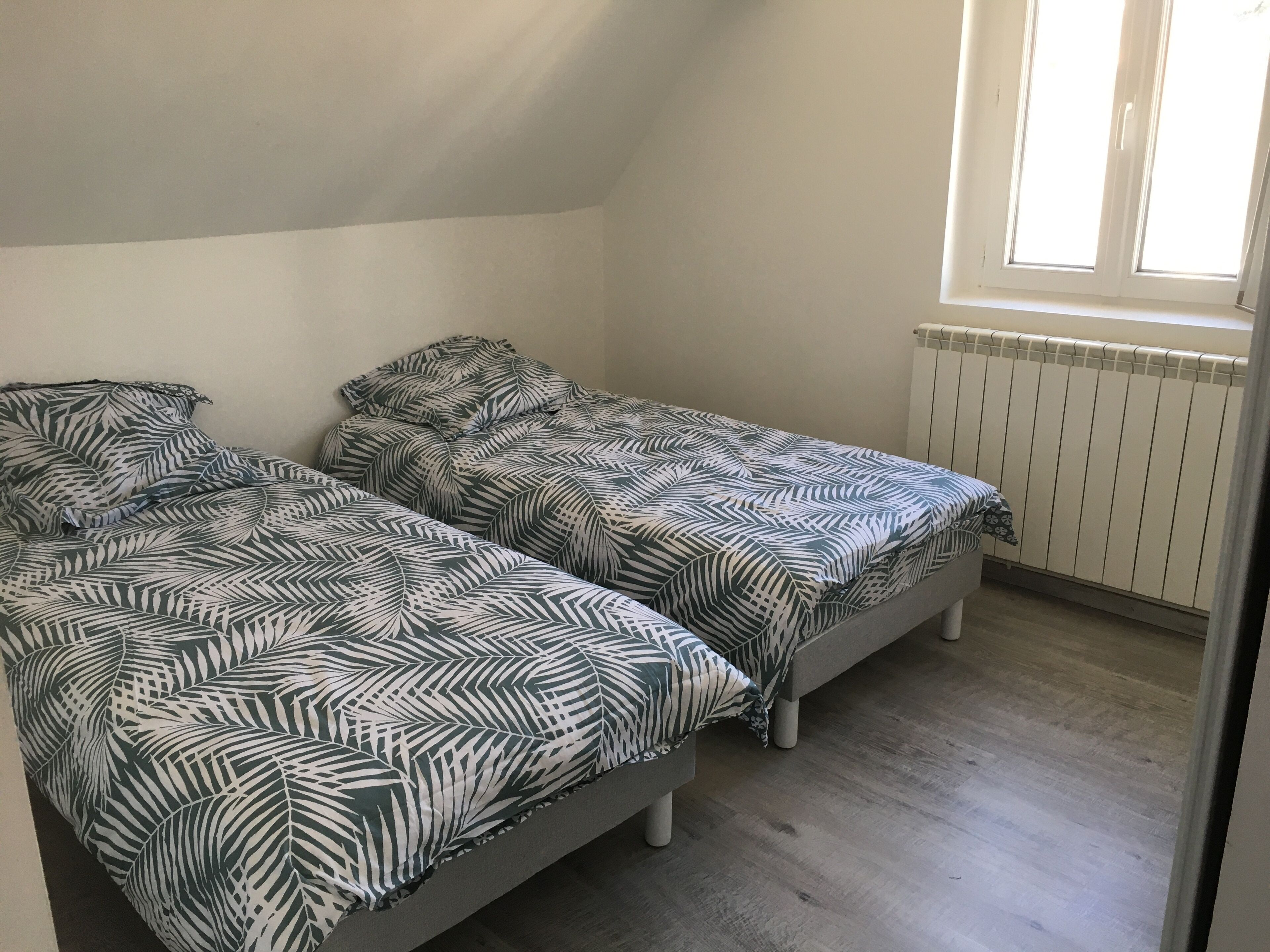 A small, single-room apartment with two twin beds, a radiator, and a window.