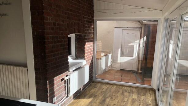 Eine kleine, offene Wohnküche mit Holzboden, weißer Arbeitsplatte und Backsteinwand.
