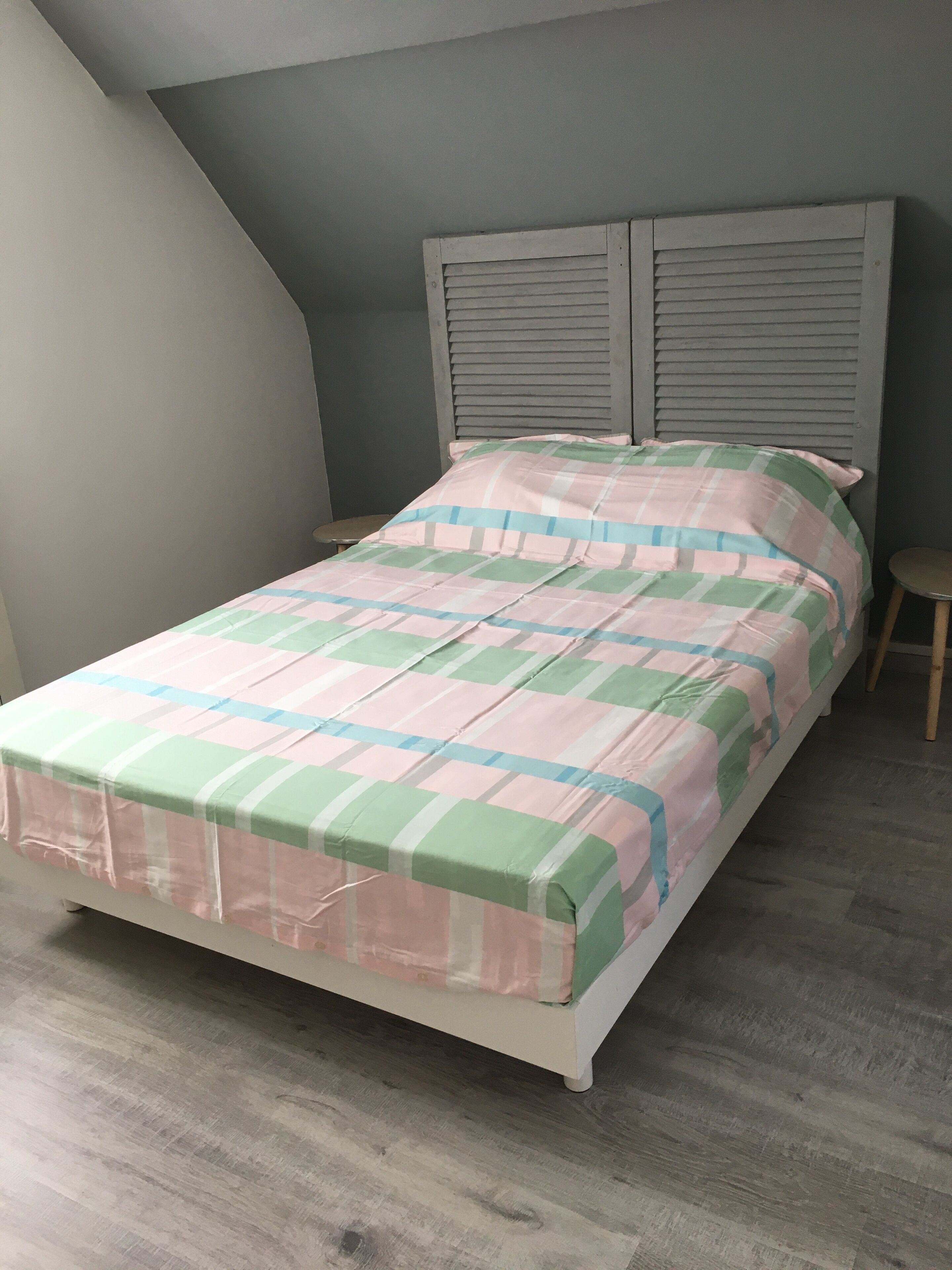 A bedroom with a bed, a nightstand, a stool, and a sloped ceiling.