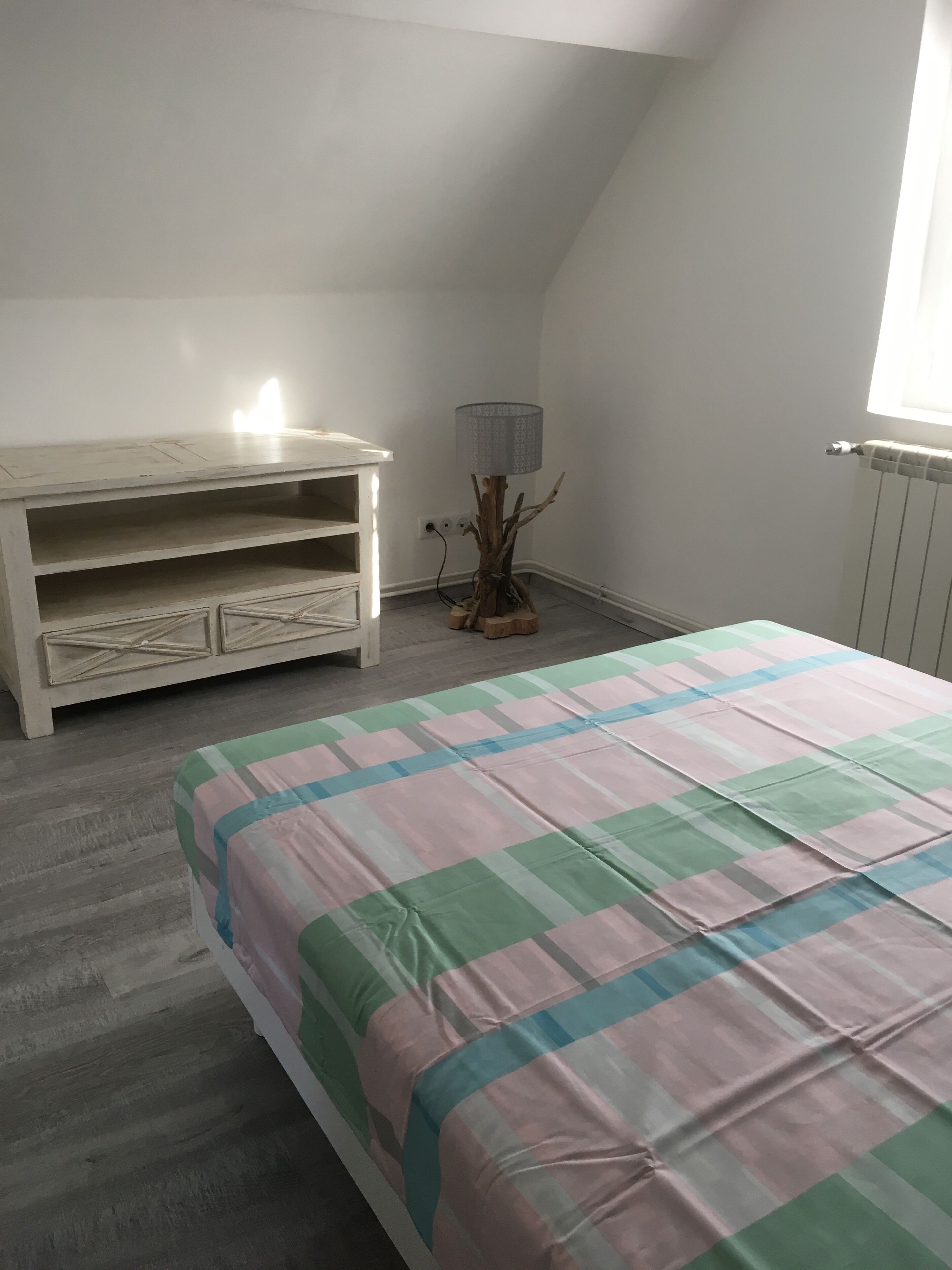 Un dormitorio con cama, cómoda, lámpara y radiador.
