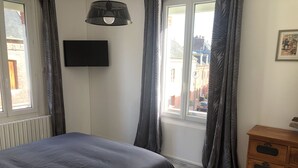 Ein Schlafzimmer mit einem Bett, einem Schminktisch, einem Fernseher und einem Fenster mit Vorhängen.