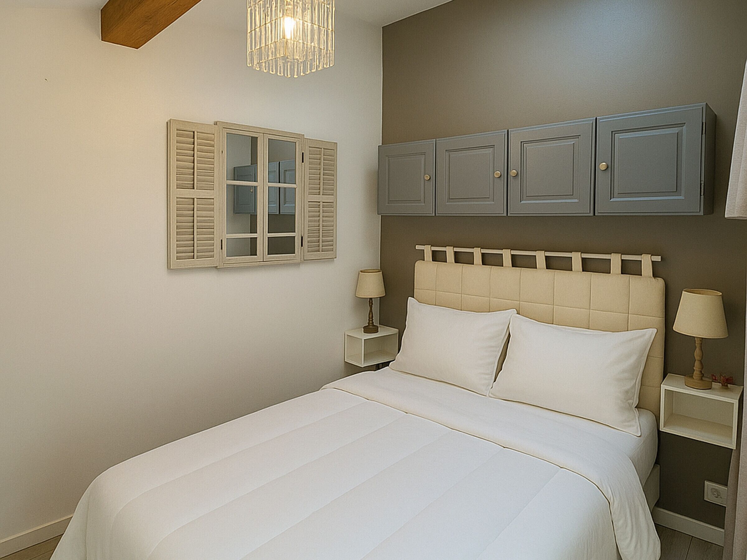A bedroom with a bed, two bedside tables, a nightstand, a hanging light fixture, and a wardrobe.