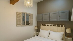 Une chambre à coucher comprenant un lit, deux tables de chevet, une commode, un luminaire suspendu et une armoire.